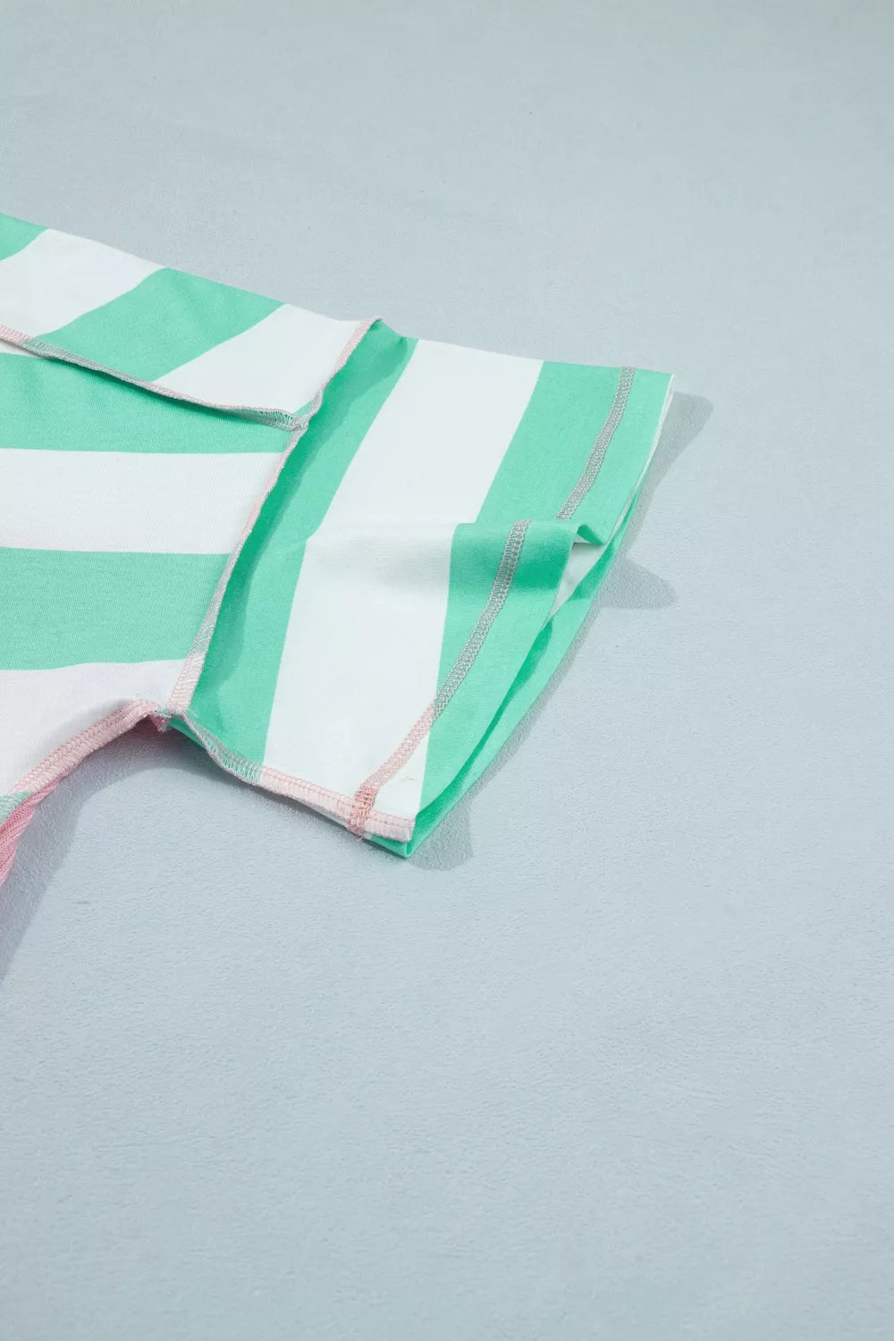 Oversized striped t-shirt in green and white with exposed seams and pink stitching detail.