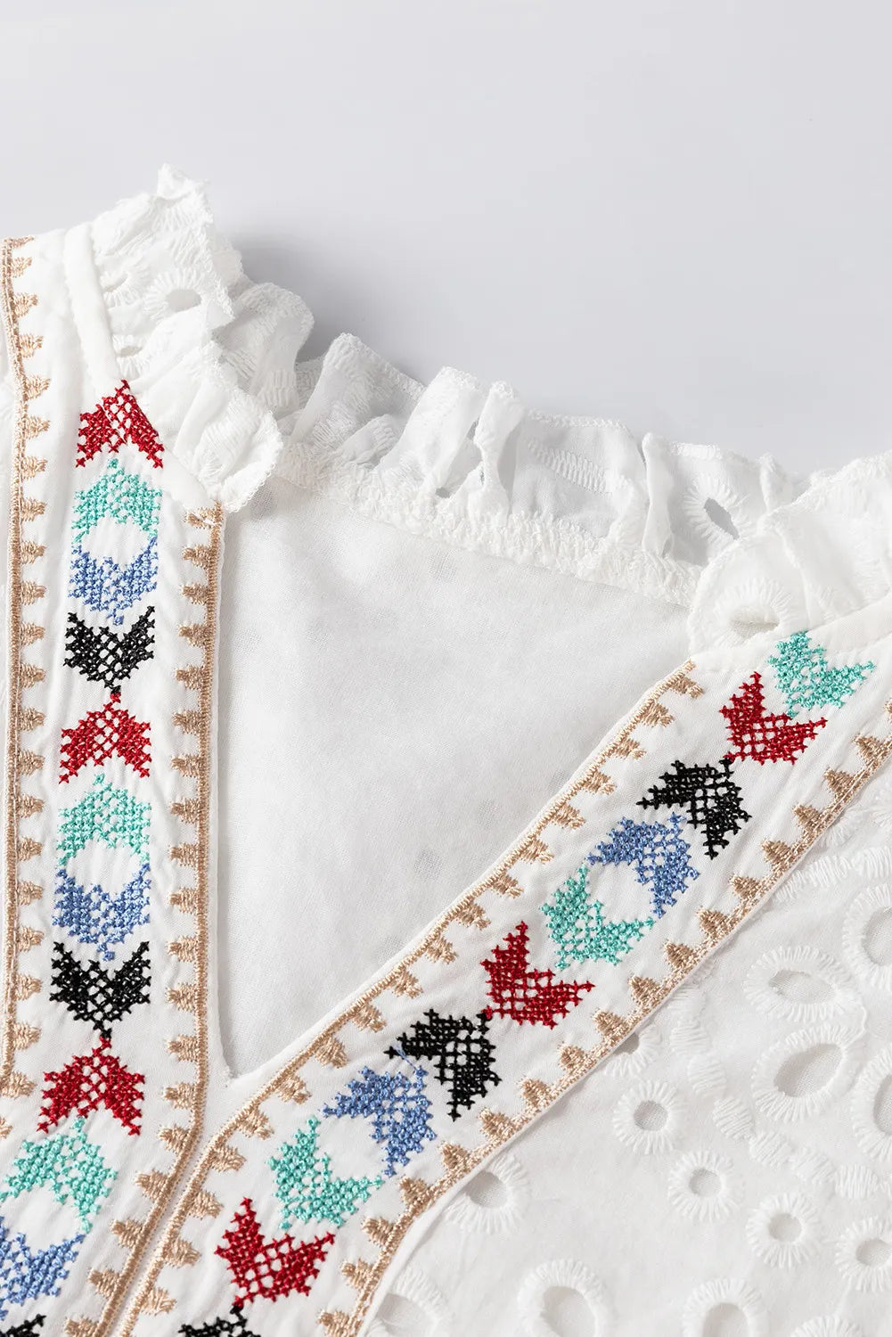 White embroidered eyelet V-neck blouse with ruffled neckline and colorful geometric trim.