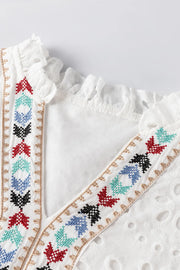 White embroidered eyelet V-neck blouse with ruffled neckline and colorful geometric trim.