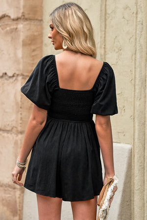 Black square neck puff sleeve romper with smocked bodice and flared skirt.