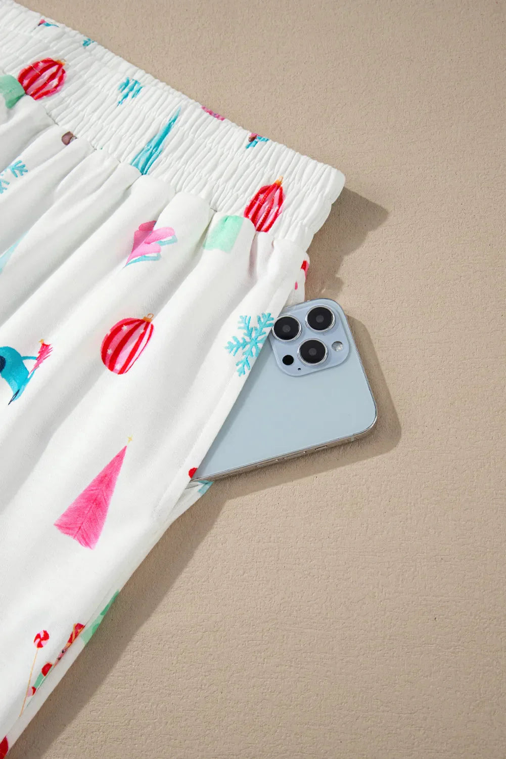 White pajama pants with festive holiday print and side pocket holding a phone.
