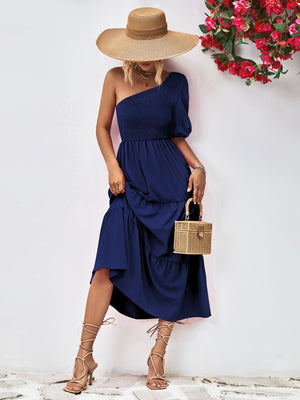 Dark blue smocked bodice one-shoulder dress with tiered skirt and puff sleeve.