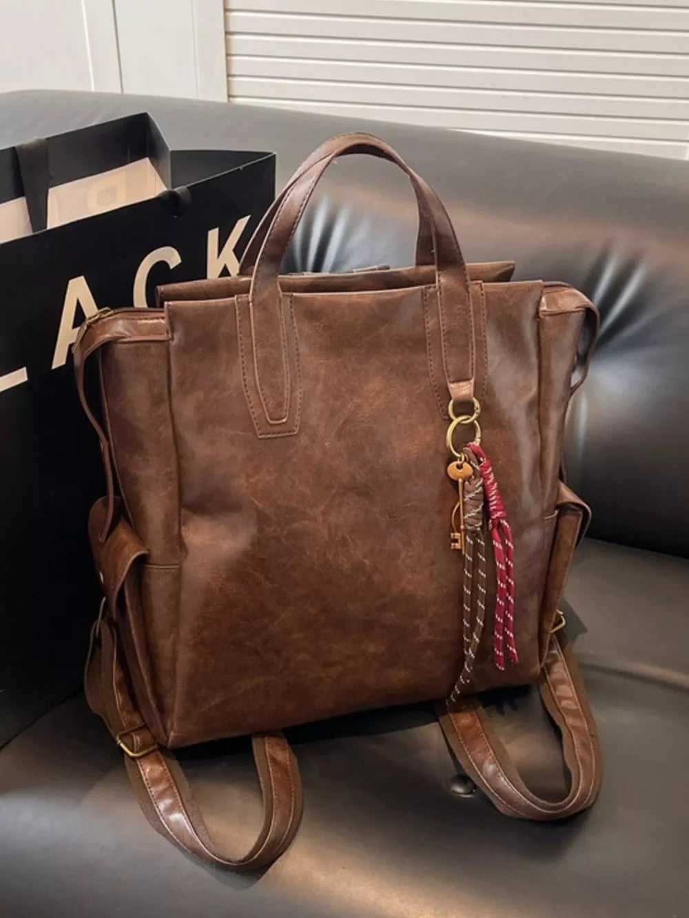 Convertible leather backpack in coffee brown with key charm and tassel detail.