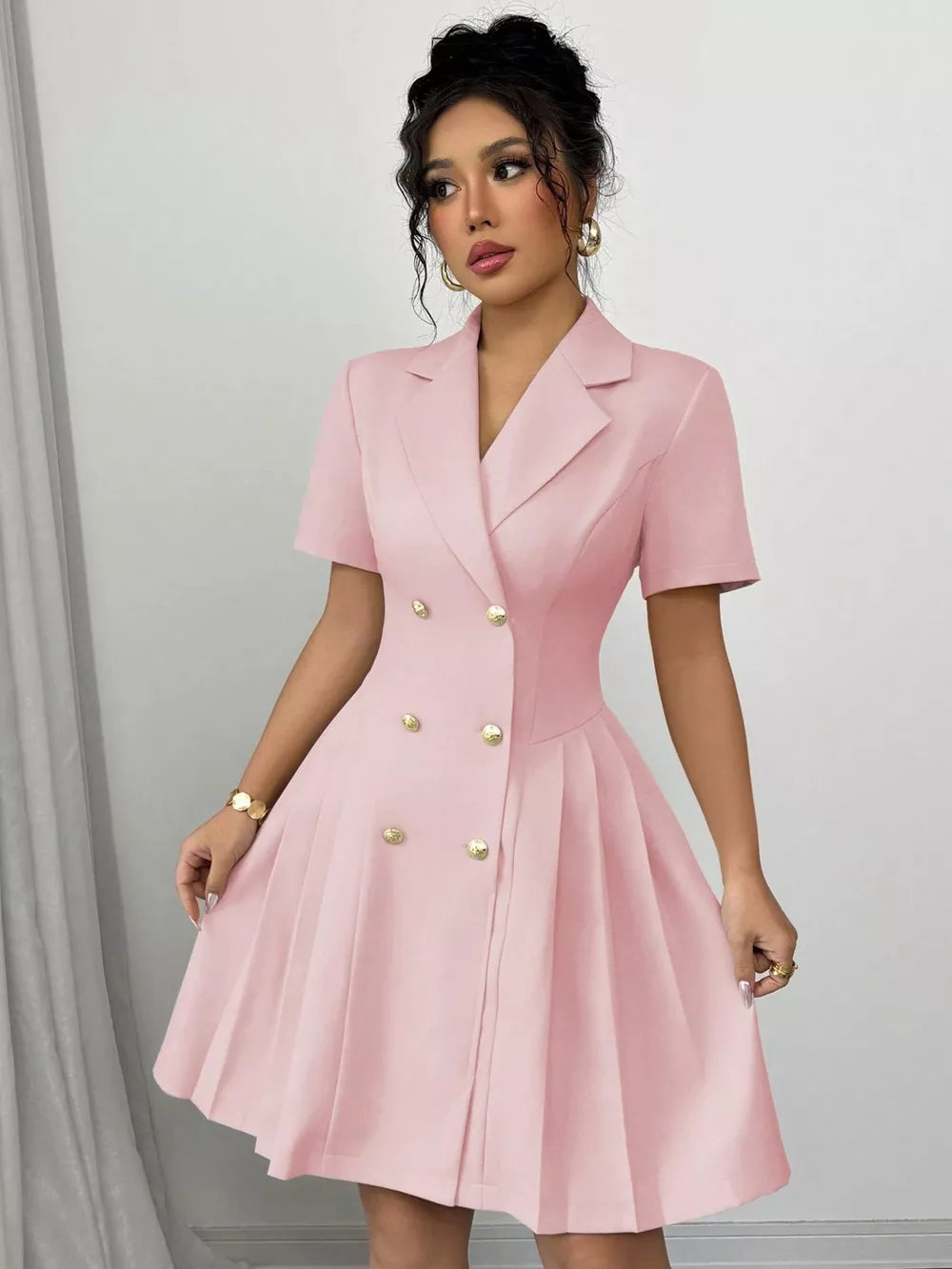 Blush pink double-breasted pleated blazer dress with gold buttons and short sleeves.
