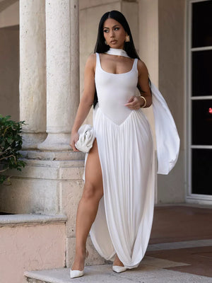 White scoop neck maxi dress with draped skirt and high slit, styled with a scarf detail.