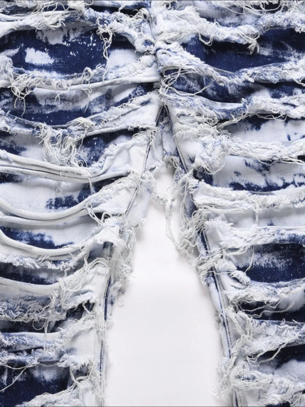 Distressed shredded denim jeans in medium wash with artistic blue tie-dye effect and frayed details.