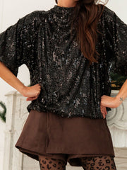Black sequin tie-back blouse with mock neck and short sleeves, styled with brown shorts.