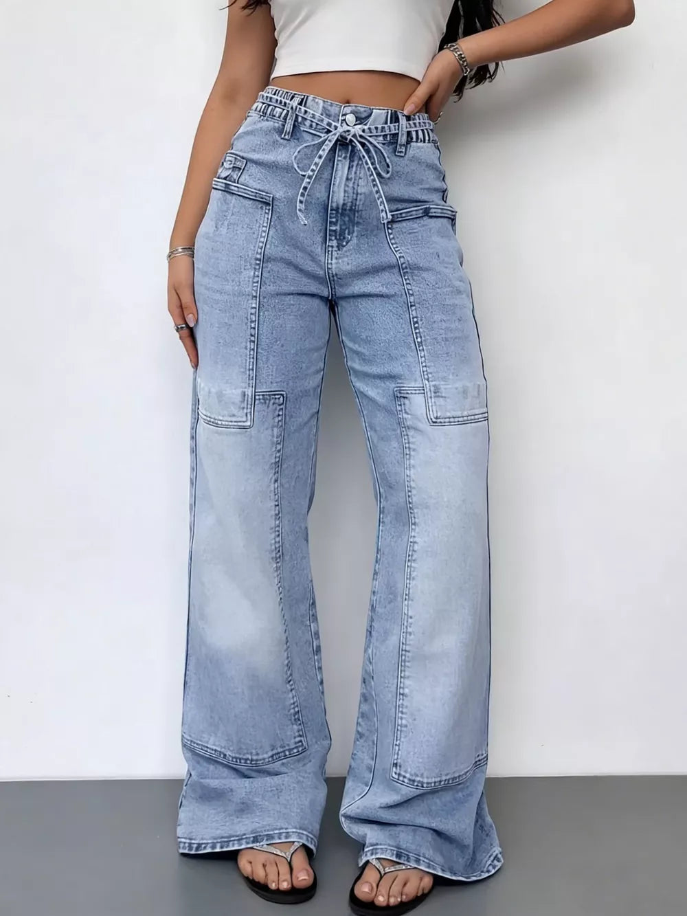 Light wash denim wide-leg cargo jeans with tie waist and utility pockets.