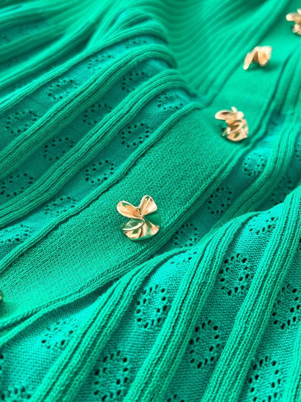 Green knit dress with eyelet details and gold buttons, close-up view.
