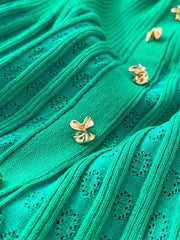 Green knit dress with eyelet details and gold buttons, close-up view.