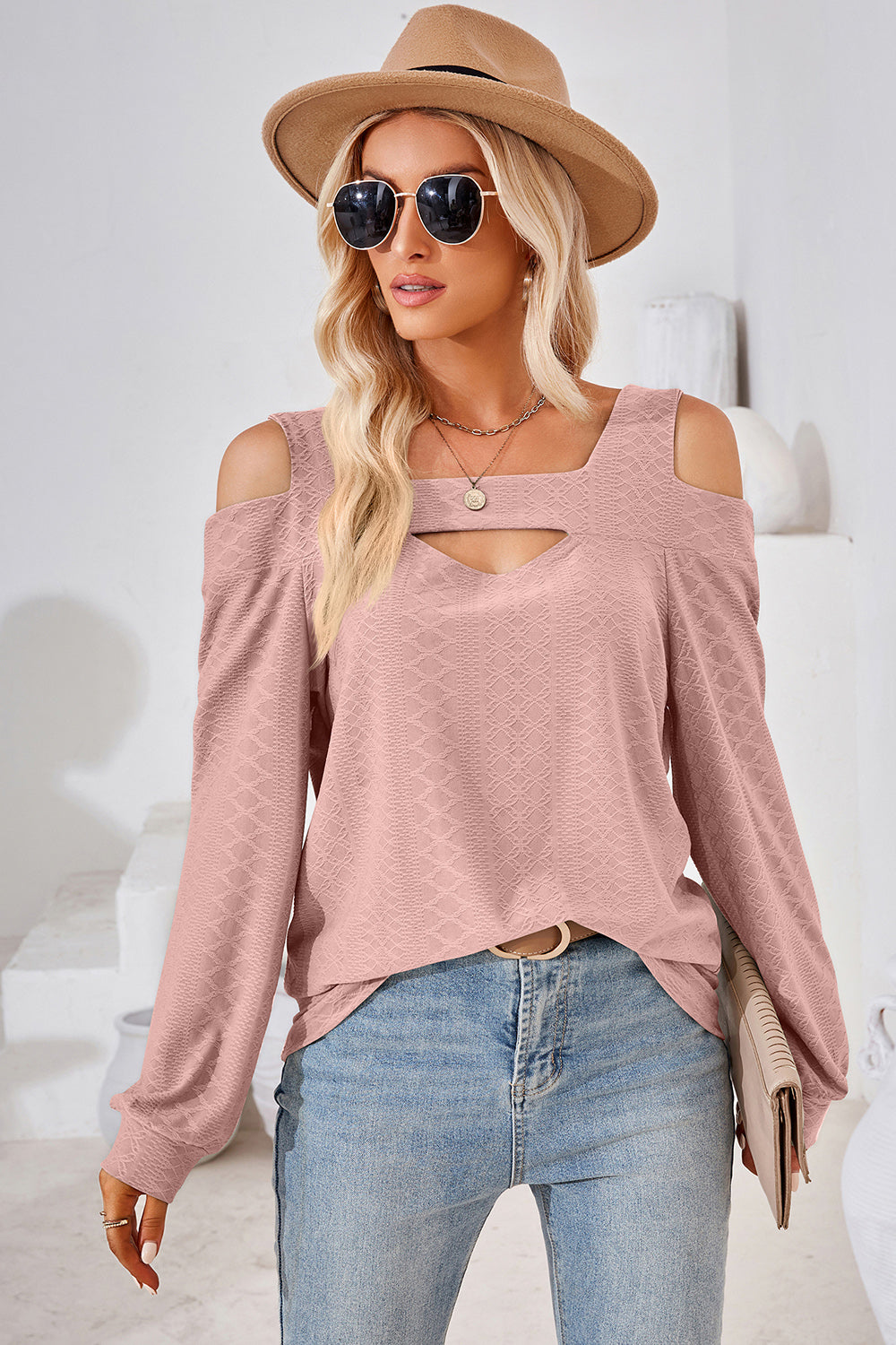 Blush pink textured blouse with cutout shoulder and neckline detail.