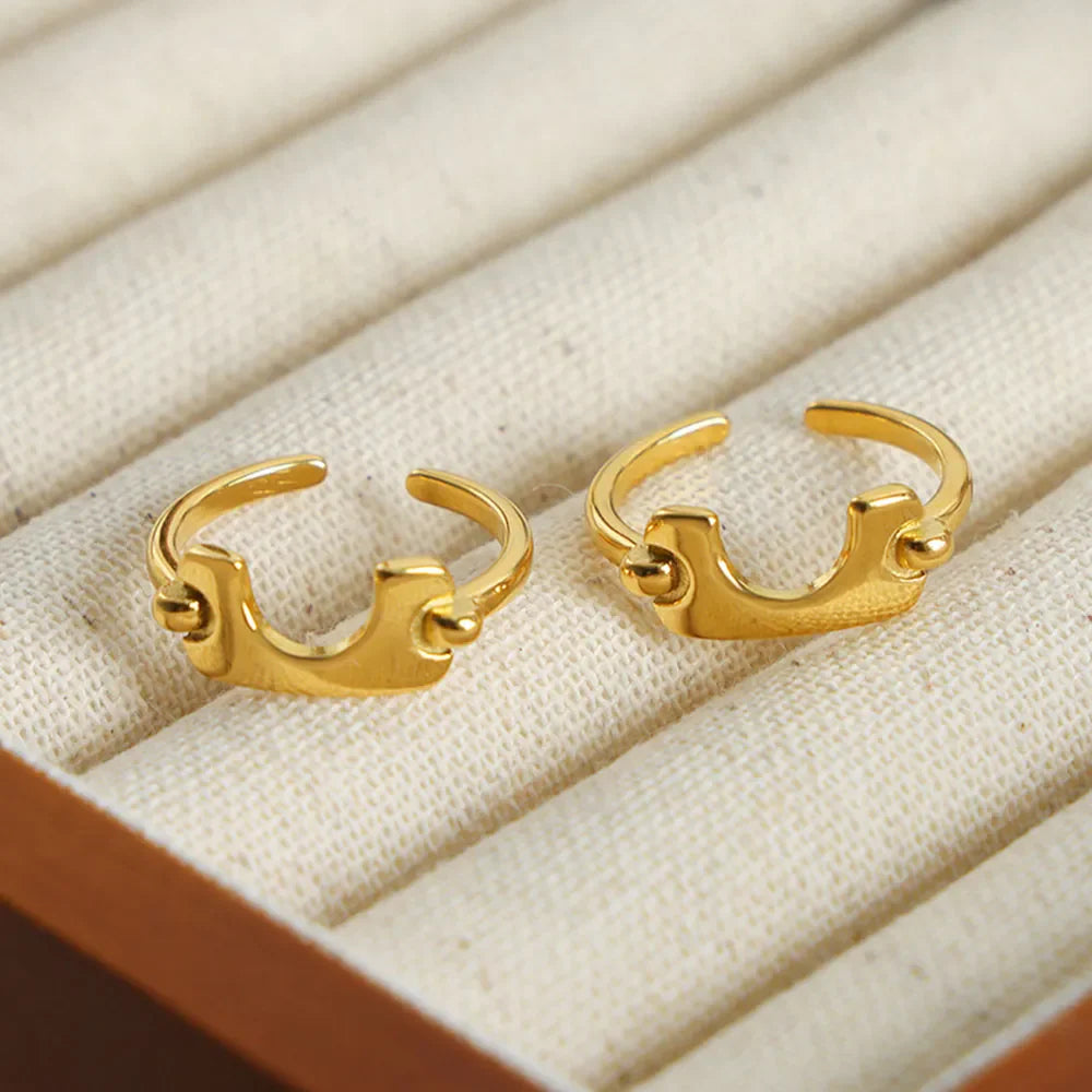 Gold open-ended ring with sculptural detail and small spheres on the ends.