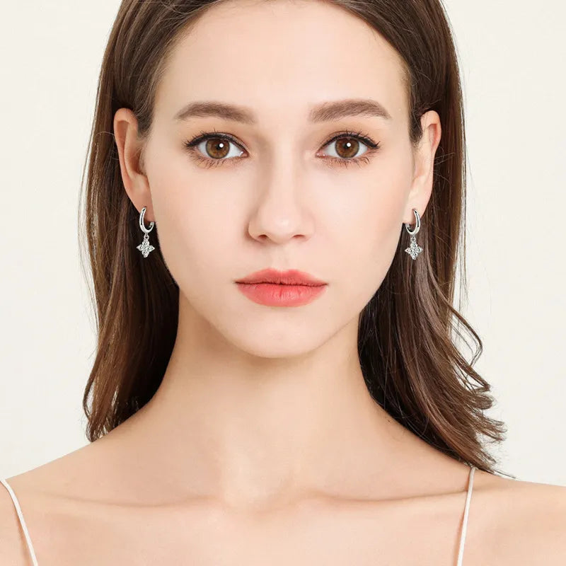 Silver huggie earrings with a dangling clover charm.
