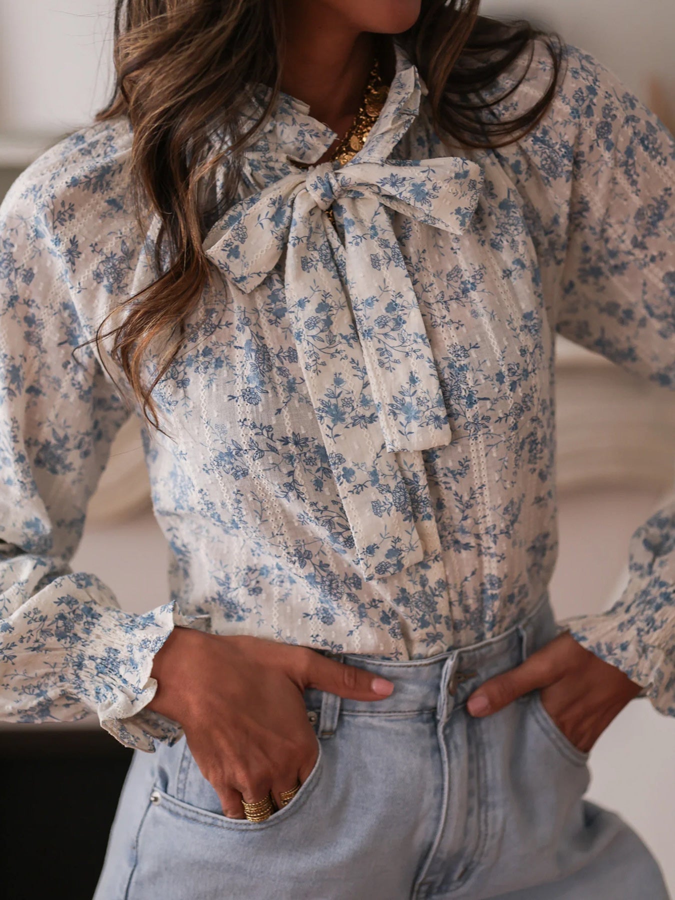 Floral tie neck long-sleeve blouse with blue floral print and ruffled cuffs.