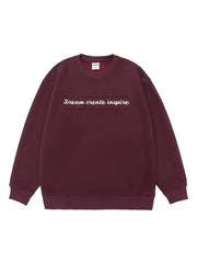 Oversized dark purple crew-neck sweatshirt with embossed text "Dream create inspire