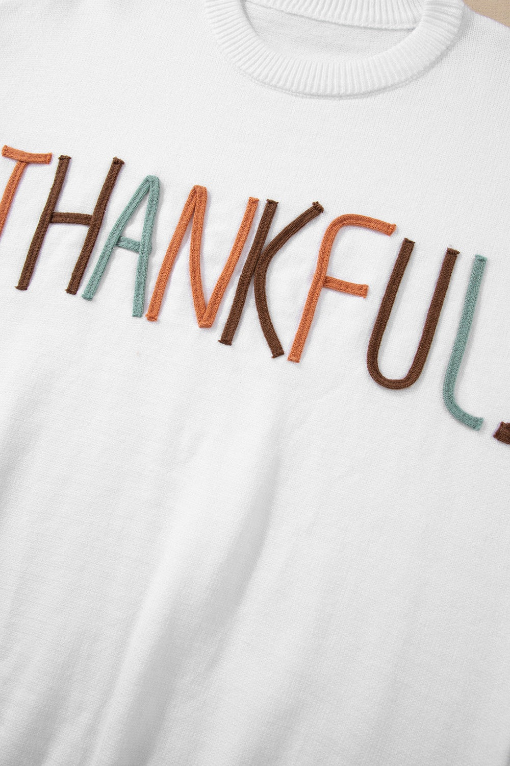 White drop shoulder sweater with "Thankful" embroidery in multi-color yarn.