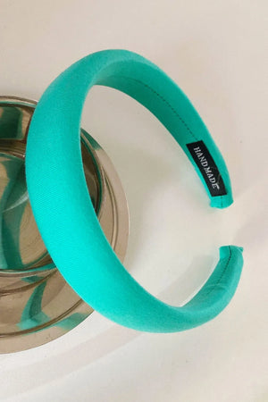 Padded turquoise headband with textured fabric and a black "HANDMADE" tag.
