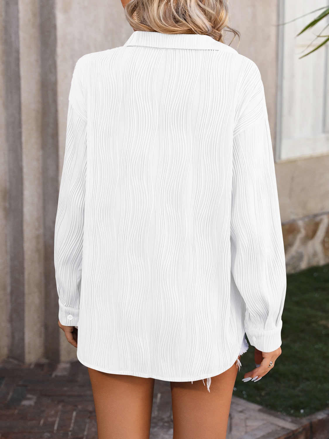 White oversized button-down shirt with textured vertical pleats and a collared neckline.