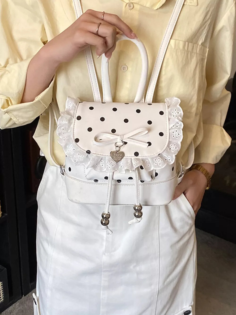 Charming white polka dot lace mini backpack with bow and heart charm detail.