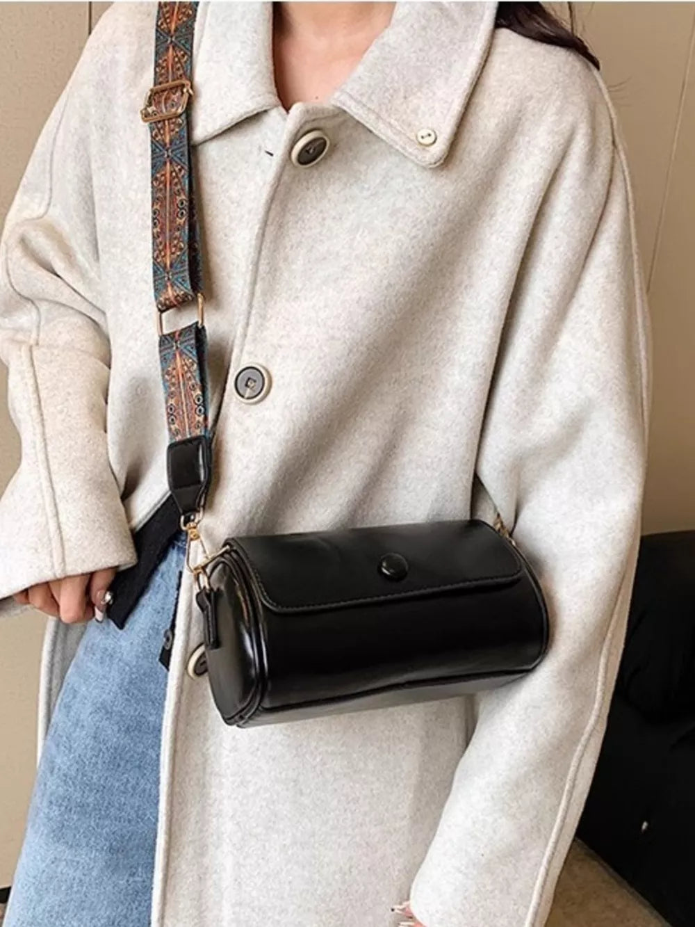 Black leather crossbody bag with ethnic strap and button closure.