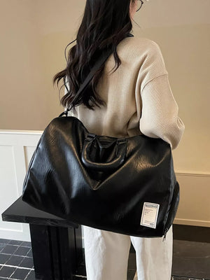 Spacious black pu leather travel duffel bag with top handles and shoulder strap.
