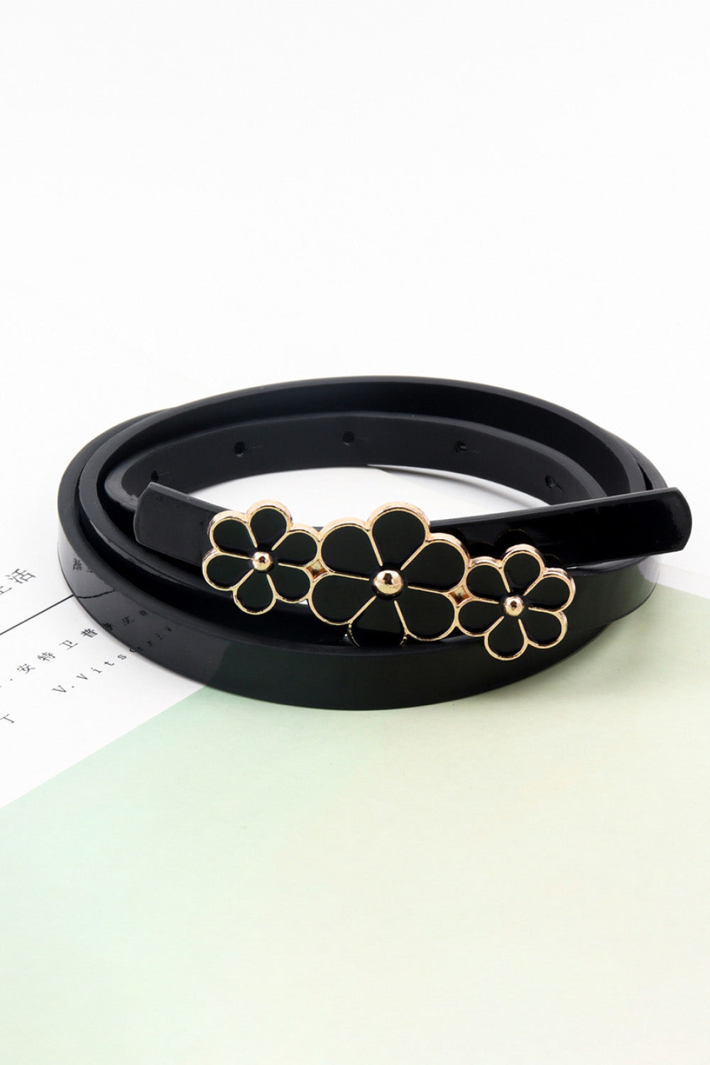 Black skinny belt with three floral charms and gold trim.
