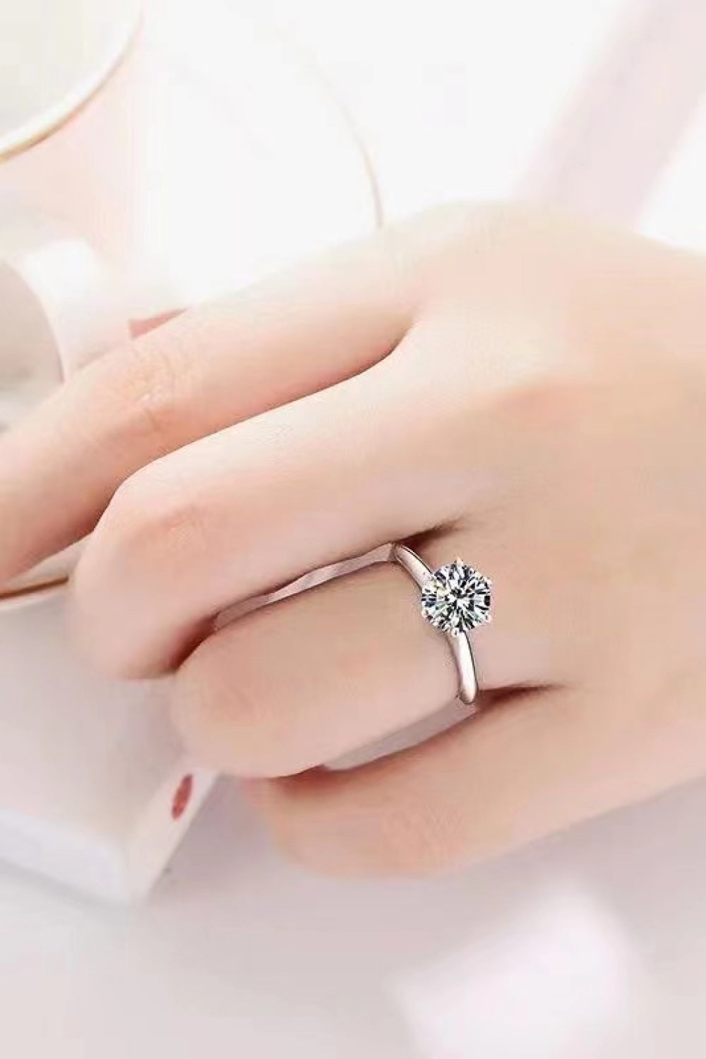 Silver ring with a brilliant cut moissanite solitaire stone on a hand.