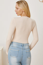 Tan ribbed long sleeve bodysuit with plunge neckline, styled with light wash jeans.