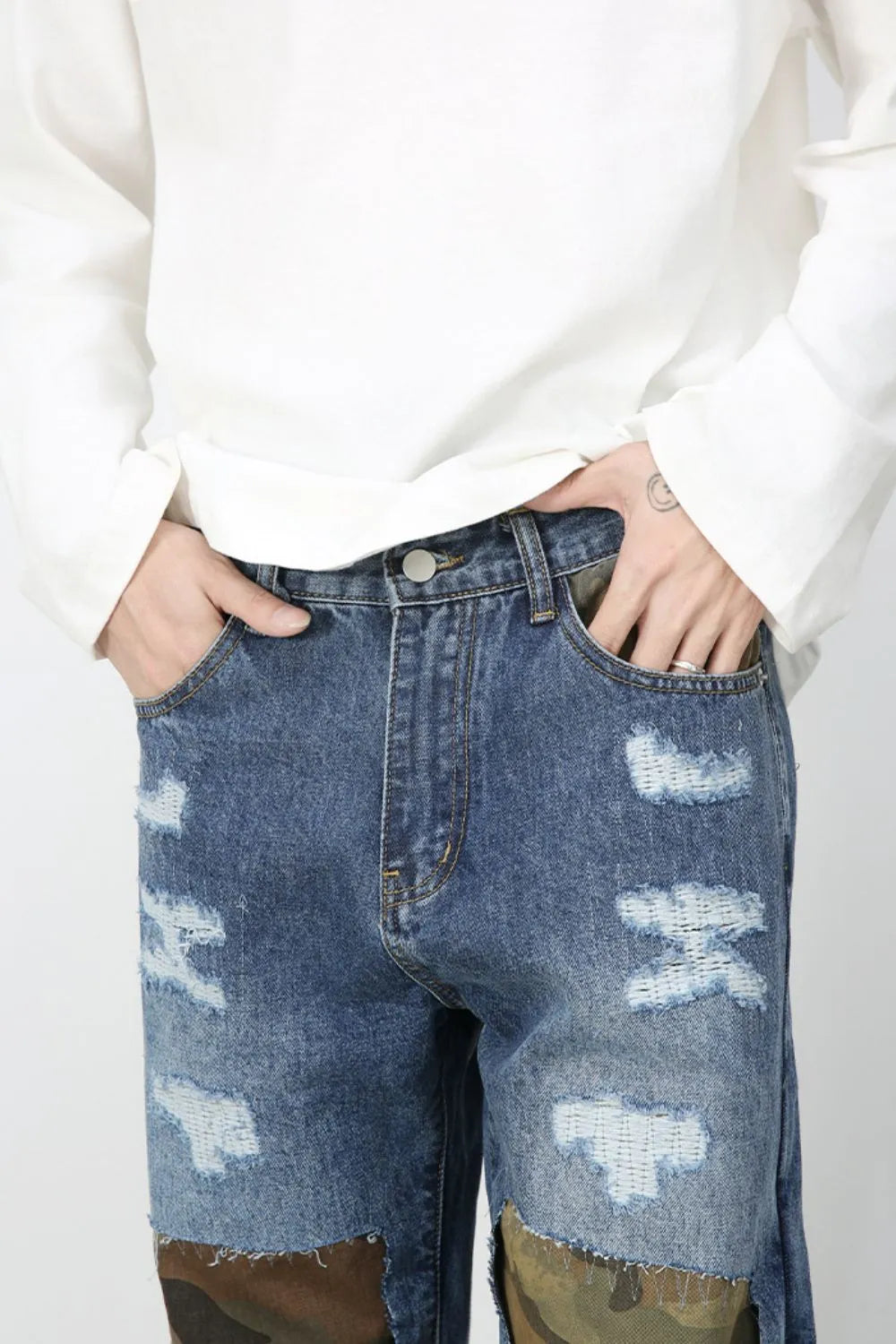 Medium wash denim jeans with camouflage patchwork and distressed details.