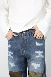 Medium wash denim jeans with camouflage patchwork and distressed details.