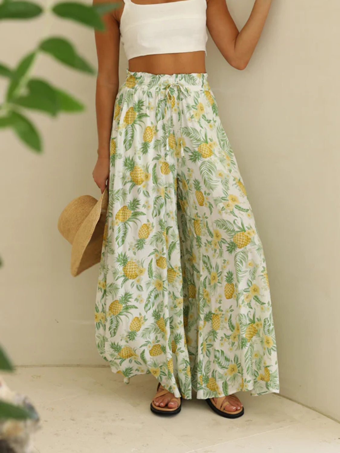 Pineapple print palazzo trousers in white with yellow and green tropical pattern, featuring a drawstring waist and wide legs.