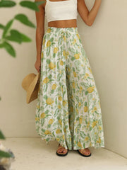 Pineapple print palazzo trousers in white with yellow and green tropical pattern, featuring a drawstring waist and wide legs.