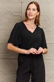 Black V-neck blouse with pleated flutter sleeves.