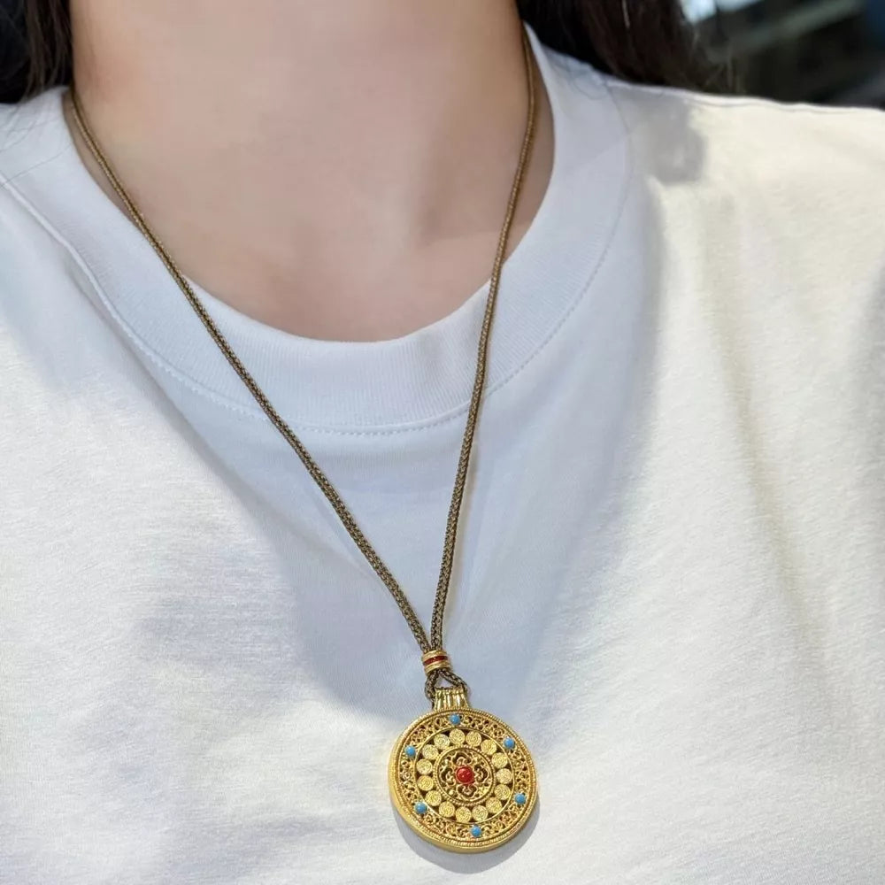 Gold-plated round pendant necklace with red and blue stones on a chain.