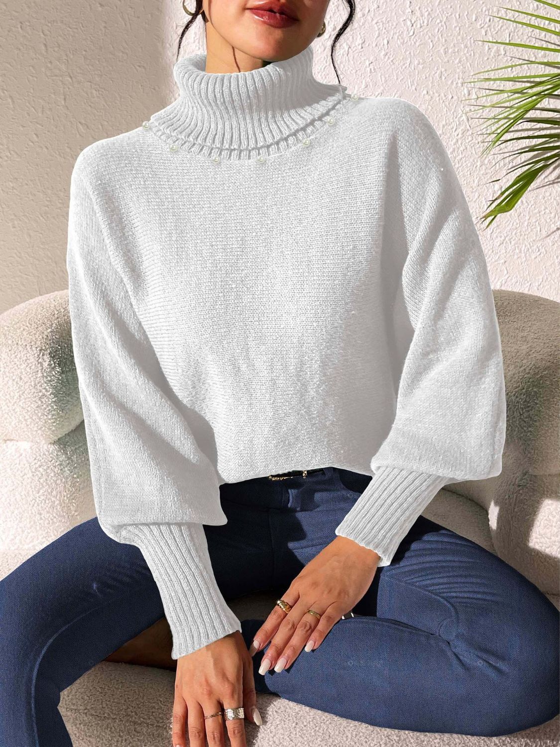 White knit turtleneck sweater with dolman sleeves and pearl embellishments at the neckline.