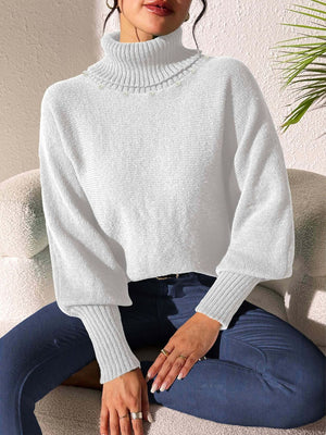 White knit turtleneck sweater with dolman sleeves and pearl embellishments at the neckline.