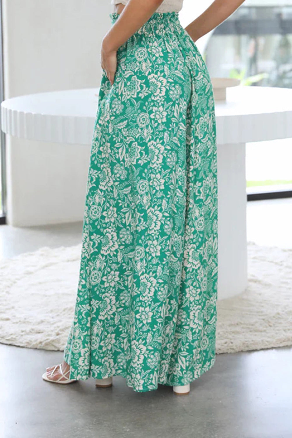 Botanical print palazzo trousers in green with a white floral pattern, featuring a wide leg and high waist.