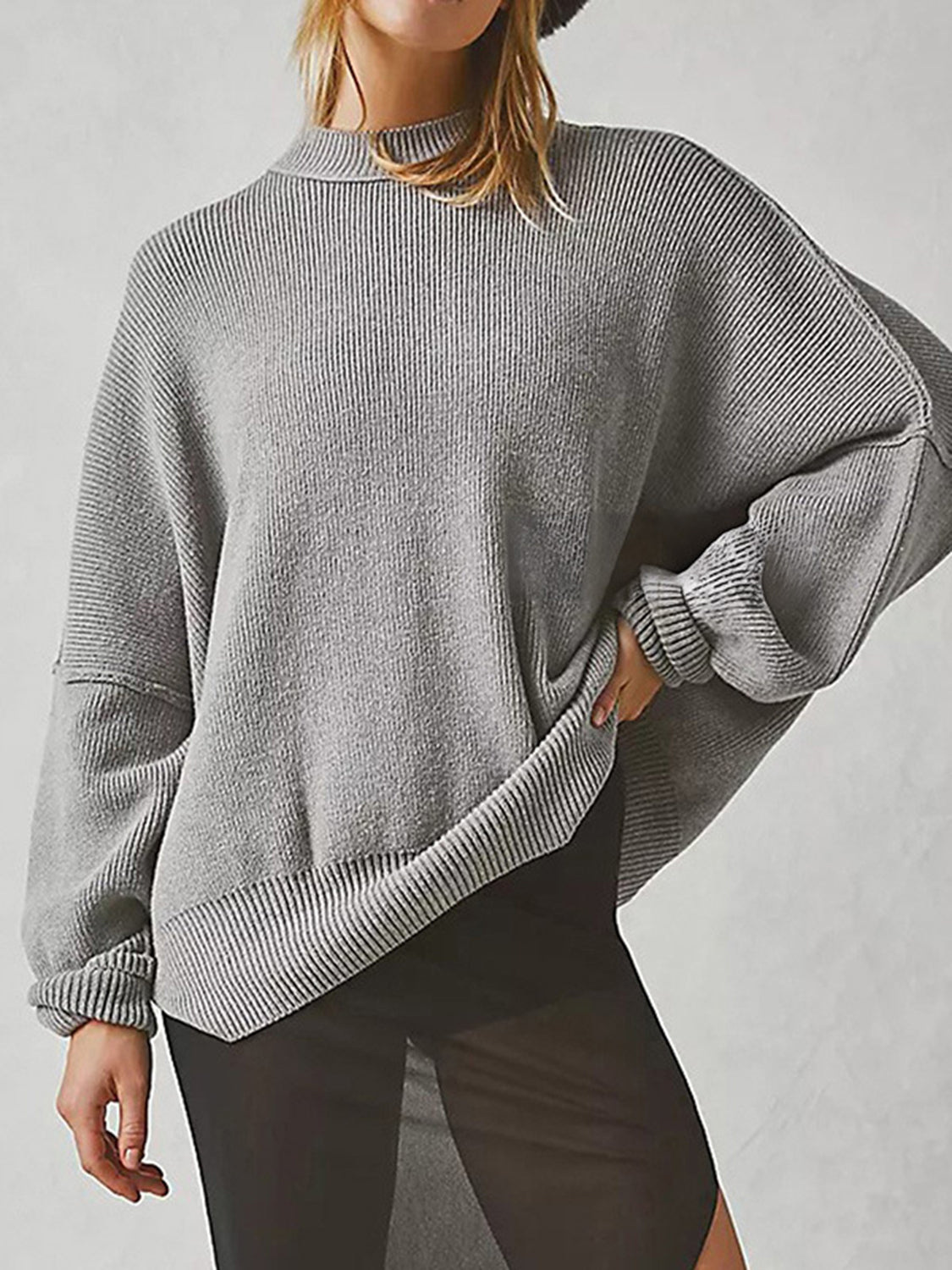 Oversized grey ribbed knit sweater with drop shoulders and mock neck, styled with sheer black pants.