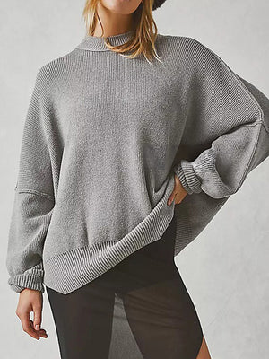 Oversized grey ribbed knit sweater with drop shoulders and mock neck, styled with sheer black pants.