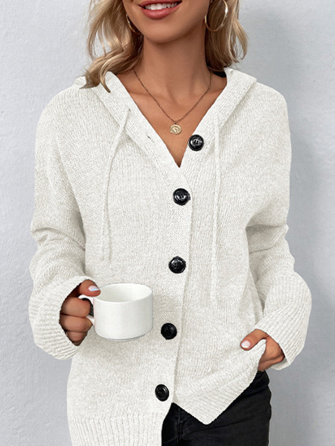 Relaxed knit hooded button-down cardigan in white with black buttons and drawstring hood.