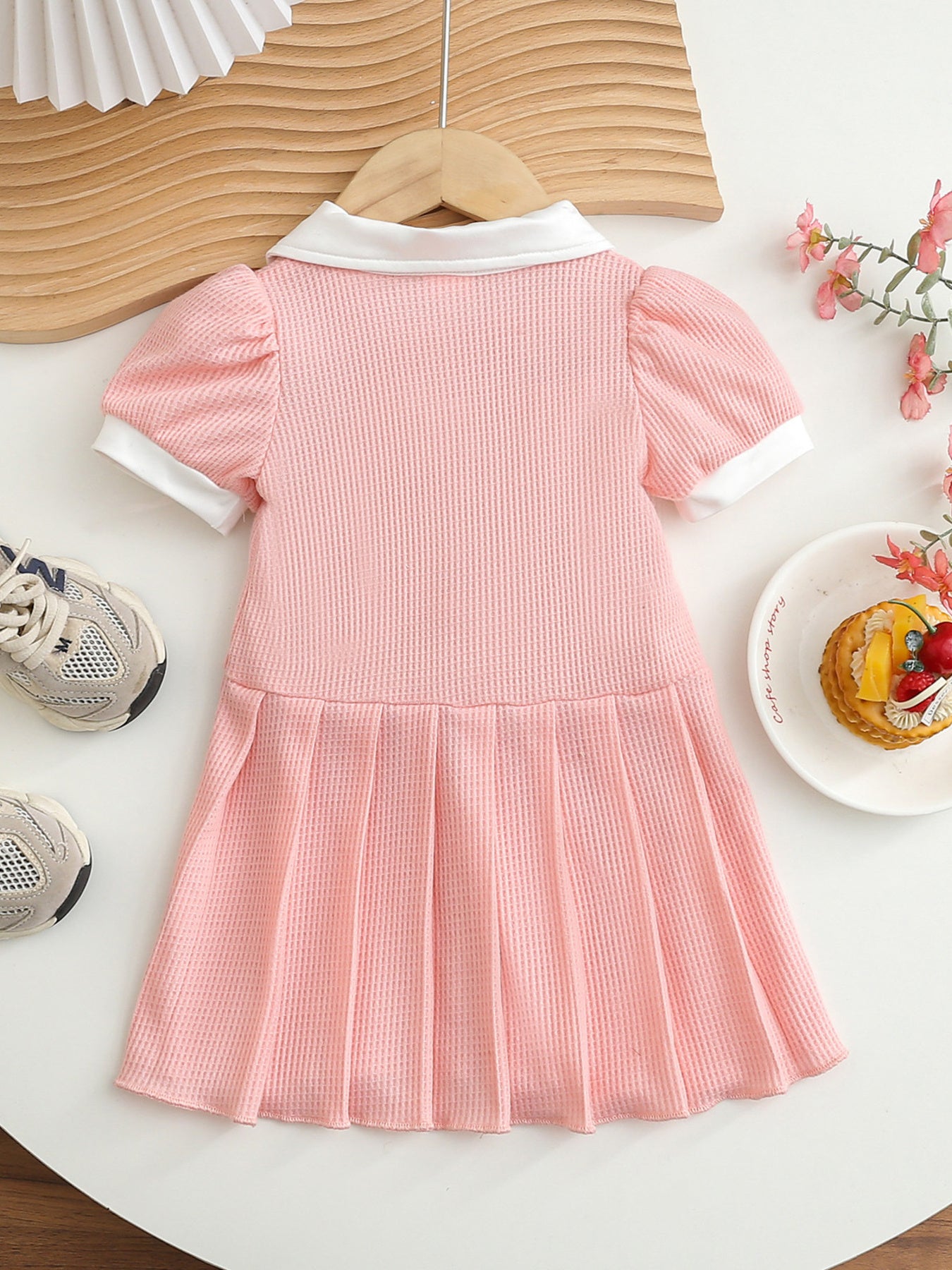 Pink baby dress with white collar and cuffs, puff sleeves, and pleated skirt.