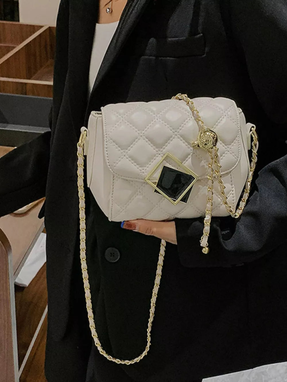 White quilted crossbody bag with gold chain strap and geometric charm detail.