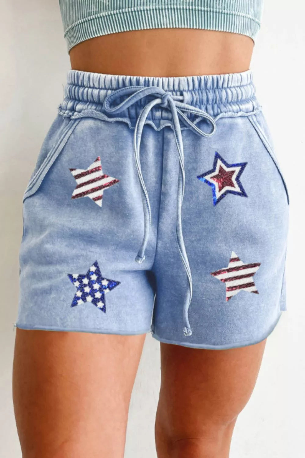Light blue cotton drawstring shorts with sequined stars pattern, elastic waistband, and raw hem.