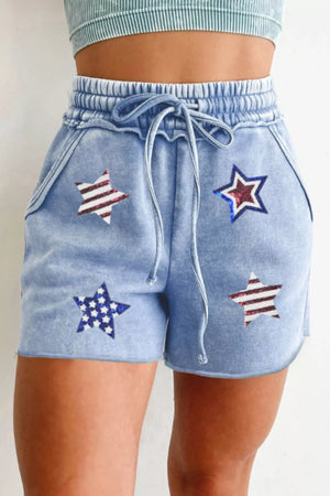 Light blue cotton drawstring shorts with sequined stars pattern, elastic waistband, and raw hem.