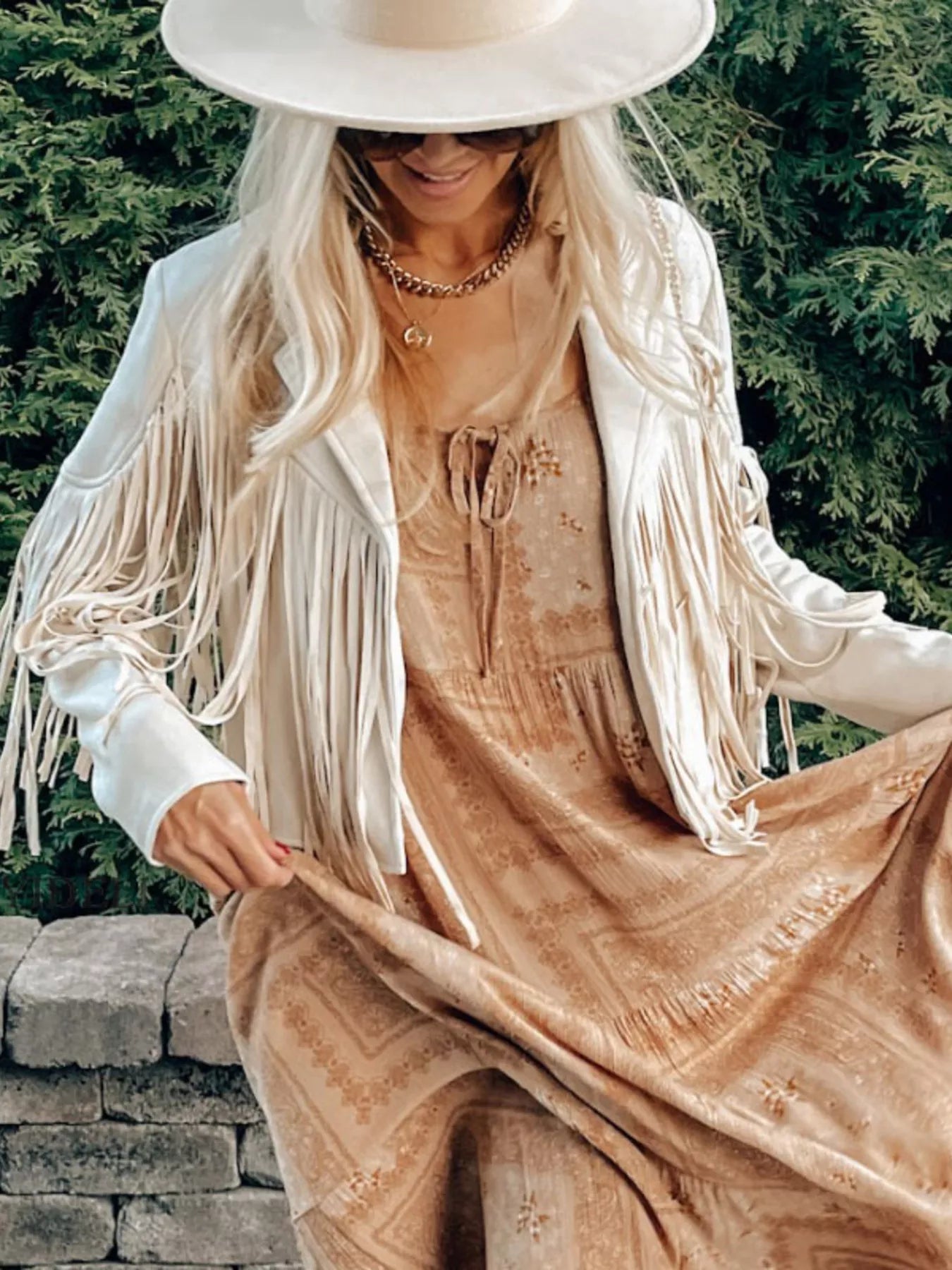 Beige fringe open front cropped jacket with a boho style, worn by a woman.