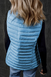 Pastel blue quilted puffer vest with horizontal quilting and fleece collar detail, worn over a black long-sleeve shirt.