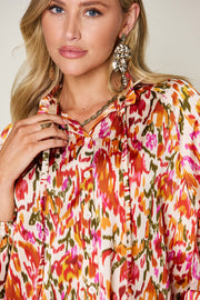 Silk tie-neck blouse with abstract ikat print in tangerine, pink, and green.