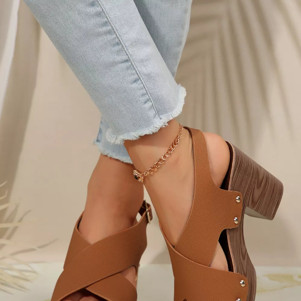 Brown crisscross high heel sandals with studs and an adjustable strap, paired with light wash jeans.