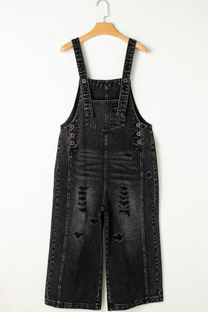 Black distressed denim culotte overalls with button closures and wide legs.