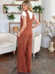 Brown wide-leg jumpsuit with deep V-neck and large front pockets, styled over a white tee.